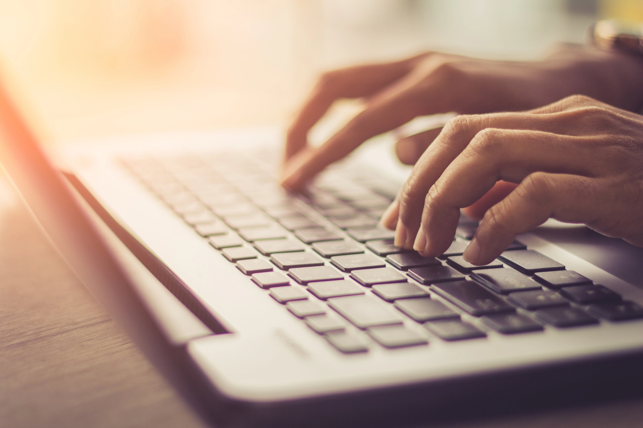 Hands of individual typing on laptop keyboard, keys being pressed, screen showing work being done.
