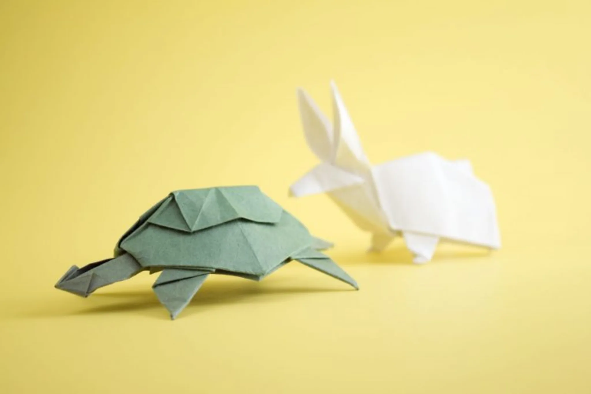 Two intricately folded origami animals displayed against a vibrant yellow background, showcasing their delicate designs