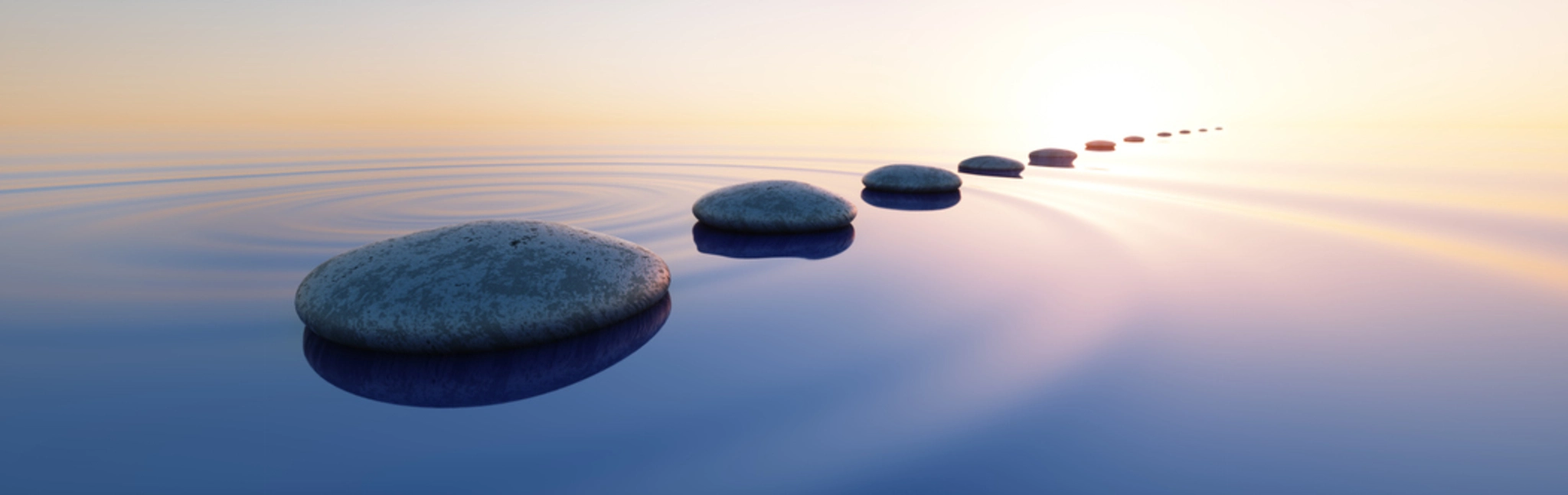 A row of rocks in the water with a sunrise in the background