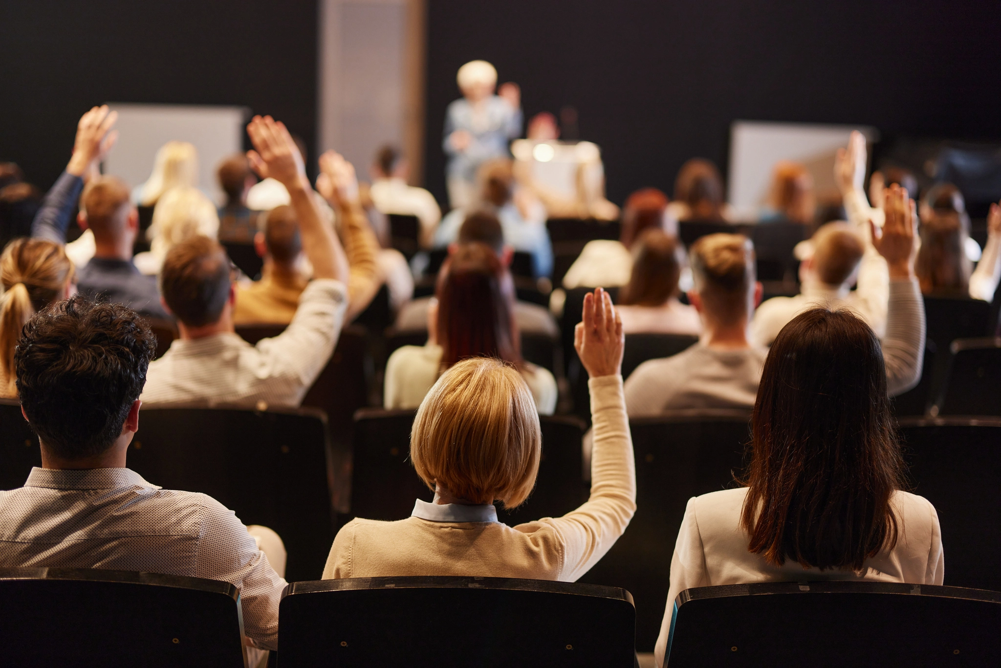A diverse group of people seated in chairs, enthusiastically raising their hands in a collaborative setting