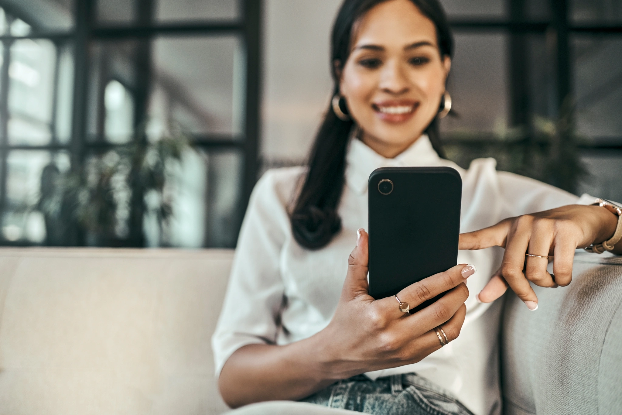 A woman on a couch, holding her cell phone, appearing relaxed and engaged in her digital activity
