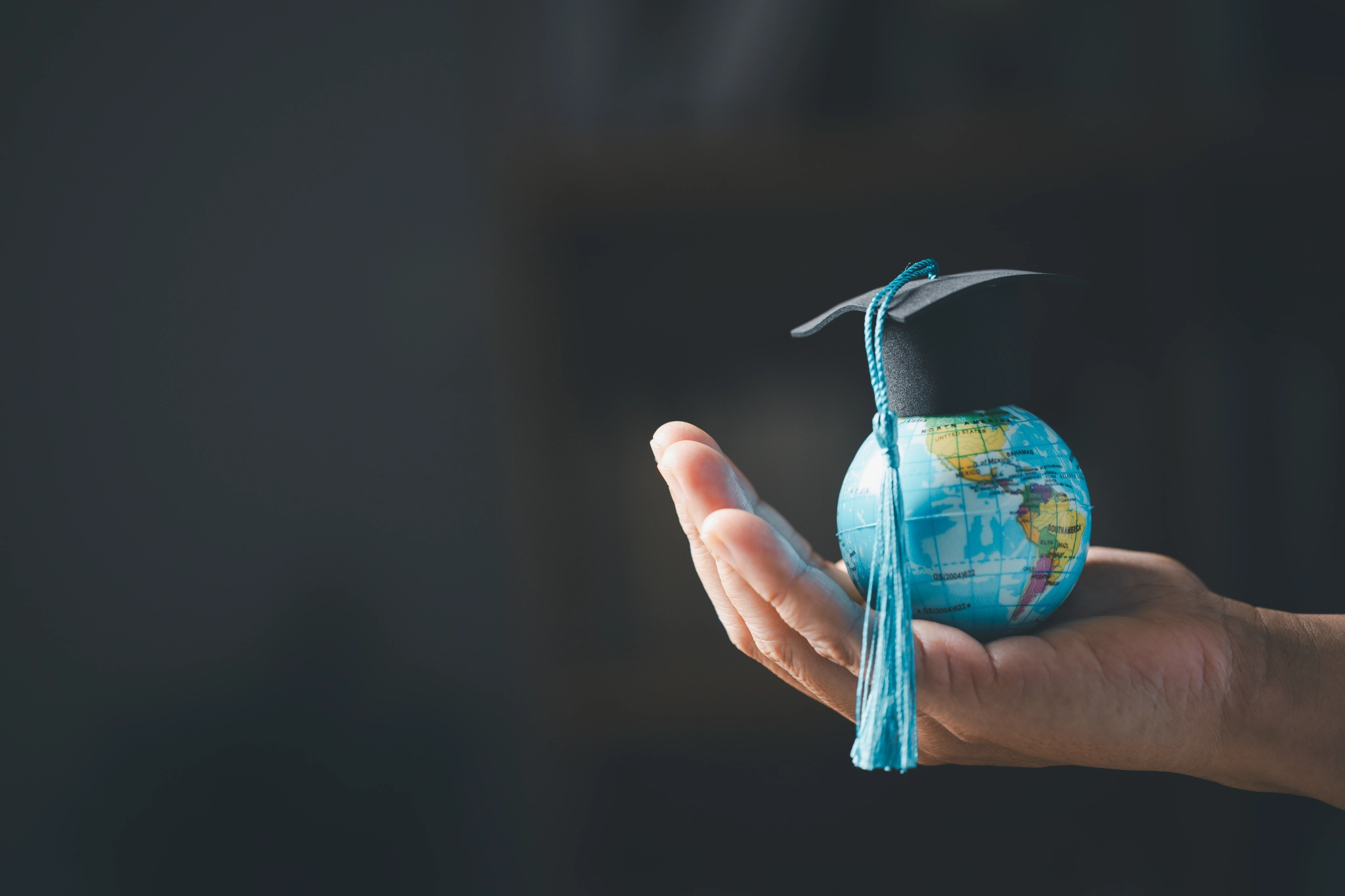 A graduation cap rests on a person's hand, which is holding a globe, symbolising education and global awareness.