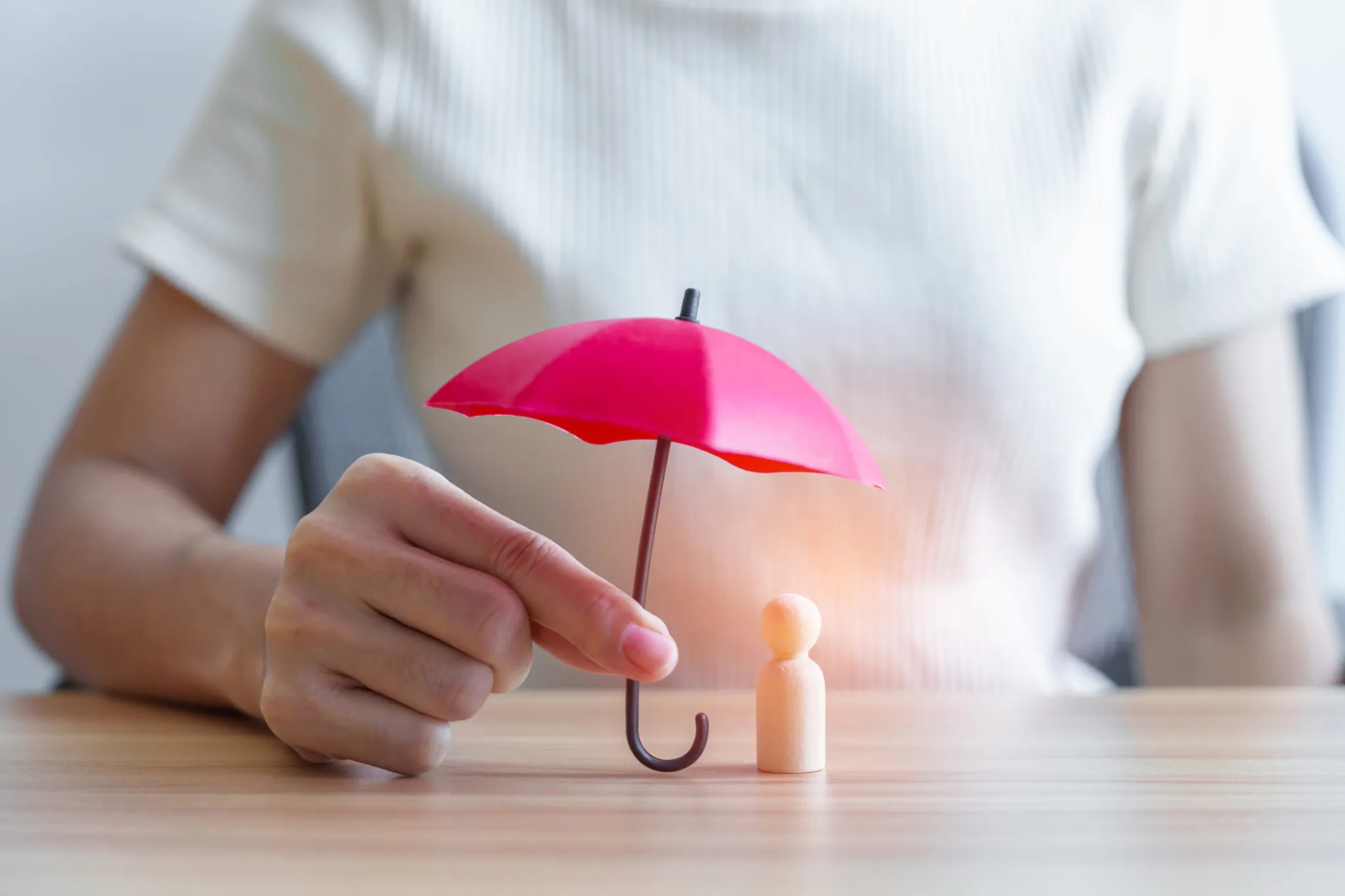 Person shielding a figurine with an umbrella in a protective gesture.